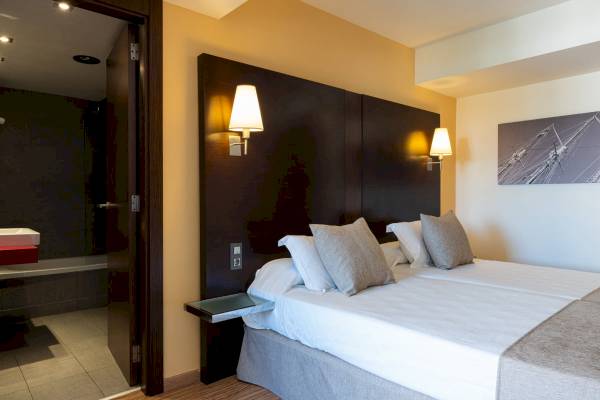 Doppelbett im Hotelzimmer des Nautic Hotel & Spa mit Nachttisch und Lampen.