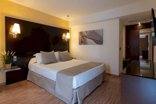 Zimmer im Nautic Hotel & Spa mit einem Bett, Kissen, einer Lampe und einem Fernseher.