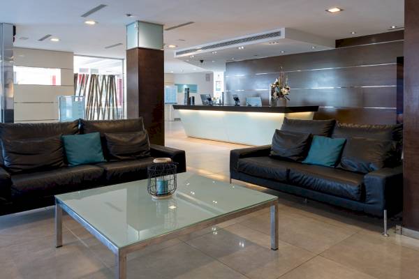 Hotellobby mit schwarzen Sofas, blauen Kissen, Glastisch und Empfangstresen.