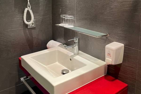 Badezimmer mit weißem Waschbecken, Edelstahlhahn und roten Möbeln am Nautic Hotel & Spa