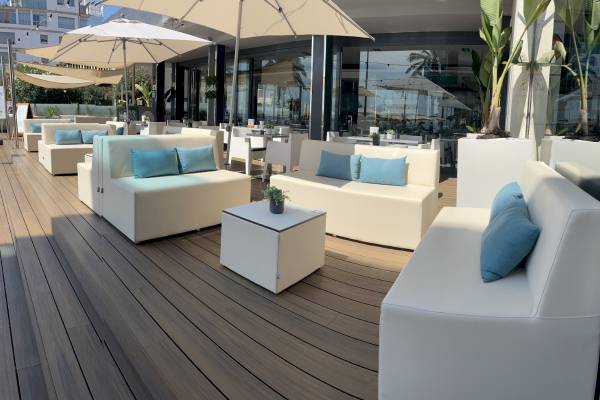 Terrasse des Nautic Hotel & Spa mit weißen Sofas und Tischen, blauen Kissen und großen Sonnenschirmen.