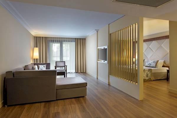 Innenbereich des Seven Seas Hotel Life mit Wohnzimmer, Couch, Sessel, Tisch, Lampe, Fernseher, und Schlafzimmer mit Bett und Kissen.