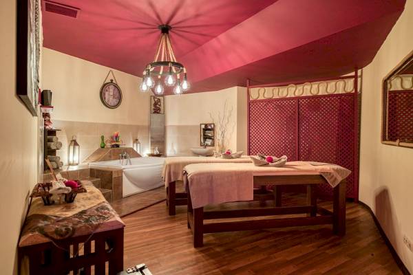 Spa-Zimmer im Seven Seas Hotel Life mit zwei Massagetischen, Badewanne und roten Decken.