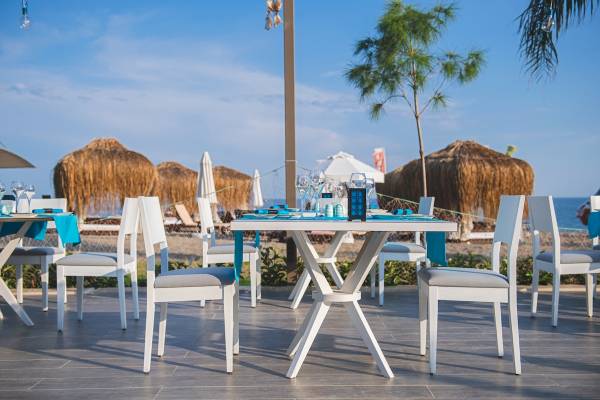 Terrasse des Seven Seas Hotel Life mit weißen Tischen und Stühlen und Blick auf den Strand.