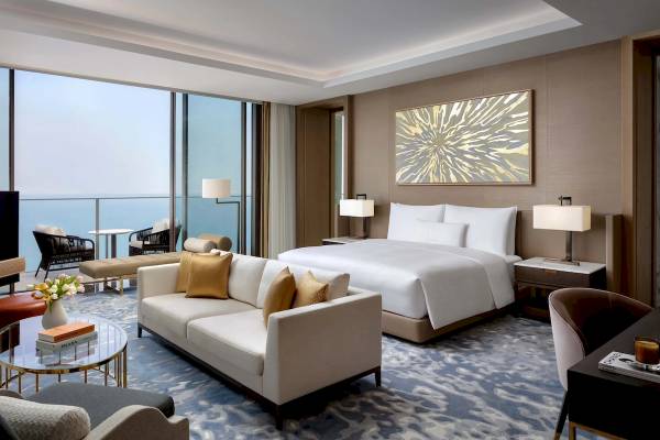 Innenansicht der Suite im Atlantis The Royal Hotel mit Meerblick, großem Bett, Sofa und Kunstwerk.