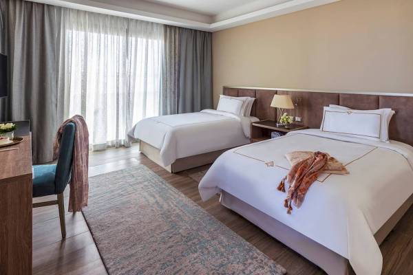 Luxuriöses Schlafzimmer mit zwei Betten, Schreibtisch, Stuhl und Teppich im Rixos Premium Magawish Suites & Villas.