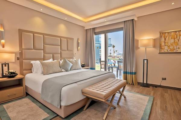 Luxuriöses Schlafzimmer im Rixos Premium Magawish Suites & Villas mit großem Bett, Kissen, und Ausblick auf den Pool.
