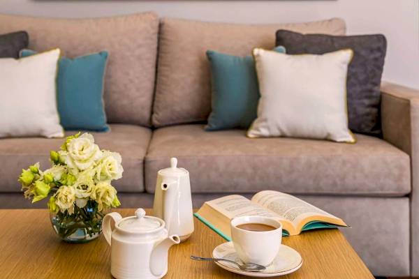 Ein Sofa mit Kissen und einem Tisch mit Teeset, Tasse, Buch und Blumen.