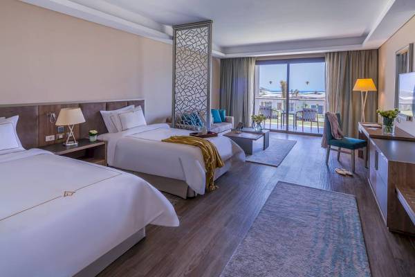Schlafzimmer des Rixos Premium Magawish Suites & Villas mit zwei Betten, Fenstern und Blick auf das Meer.