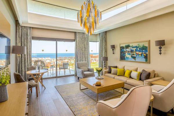 Wohnzimmer im Rixos Premium Magawish Suites & Villas mit Meerblick, großem Fenster, Couch, Teppich und Dekoration.