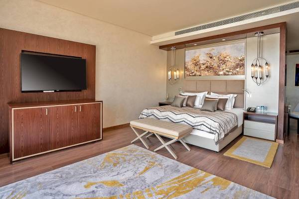 Schlafzimmer des Rixos Premium Magawish Suites & Villas mit einem großen Bett, Fernseher und Dekor.