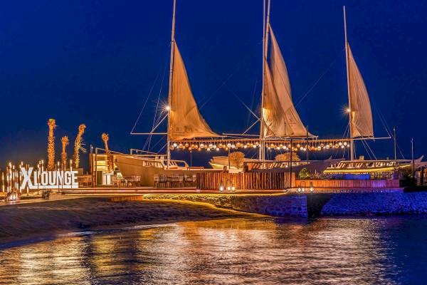 Nachtansicht des Rixos Premium Magawish Suites & Villas mit beleuchteten Segeln und Loungebereich am Wasser.
