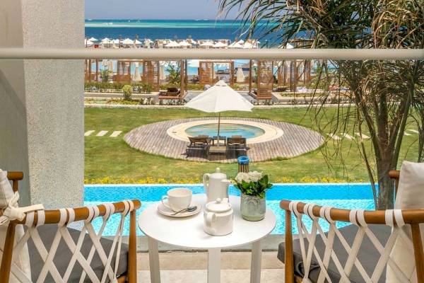 Terrasse mit Meerblick im Rixos Premium Magawish Suites & Villas mit Pool, Sonnenliegen und weißem Schirm.
