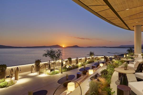 Abendlicher Ausblick vom Restaurant des Mandarin Oriental, Costa Navarino mit Sonnenuntergang über dem Meer und beleuchteten Tischen und Stühlen.