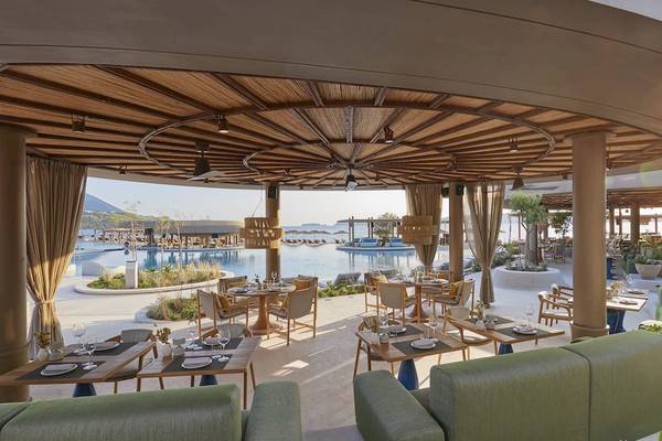 Außenbereich des Mandarin Oriental, Costa Navarino Hotels mit Esstischen und Stühlen, umgeben von einem Pool und Pflanzen.