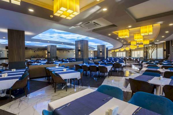 Innenansicht des Restaurants im Eftalia Ocean Hotel mit blauen Tischen und Stühlen, gelben Deckenleuchten und einer blauen Himmelsprojektion.