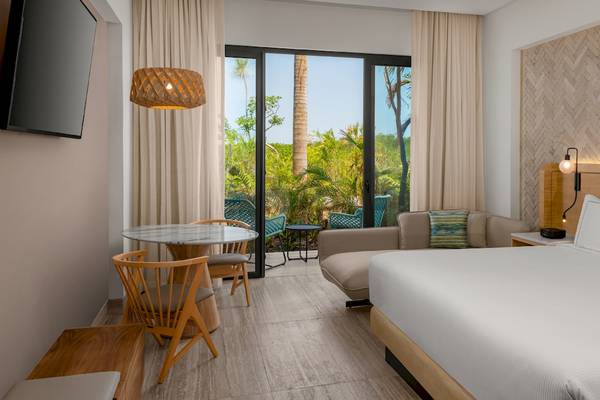 Innenansicht eines Zimmers im Hilton Tulum Riviera Maya All-Inclusive Resort mit Bett, Tisch und Sofa.
