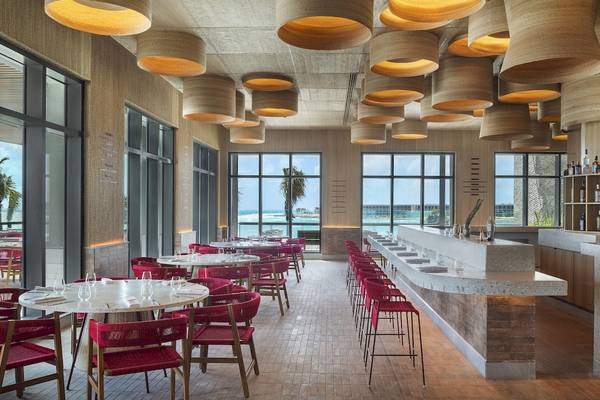 Innenansicht des Restaurants im Hilton Tulum Riviera Maya All-Inclusive Resort mit roten Stühlen und Tischen, großen Fenstern und einer Theke.