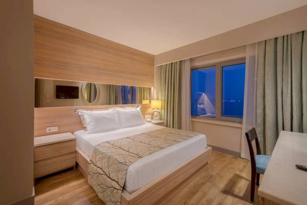 Innenansicht eines Hotelzimmers im Melas Resort mit einem Bett, Nachttisch, Spiegel und Fenster.