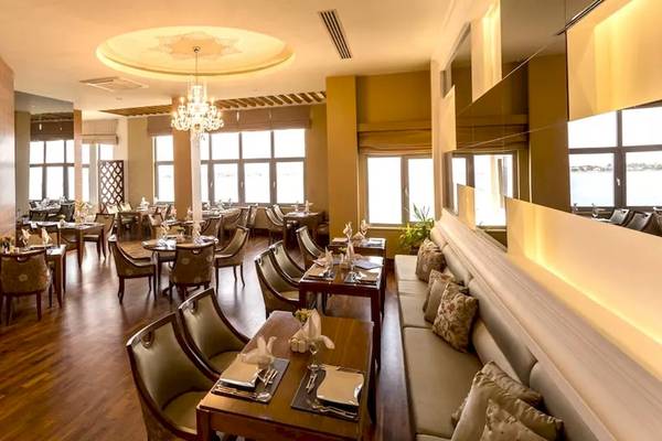 Innenansicht des Restaurants im Melas Resort mit Holzböden, Tischen, Stühlen und einer großen Fensterfront.