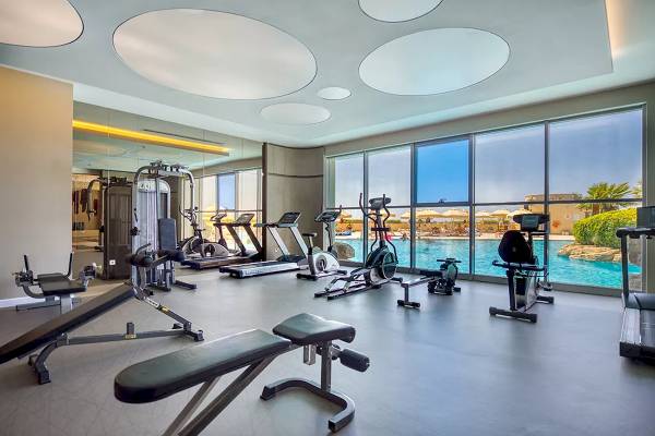Fitnesscenter-Innenbereich im Melas Resort mit großen Fenstern, die auf einen Pool blicken