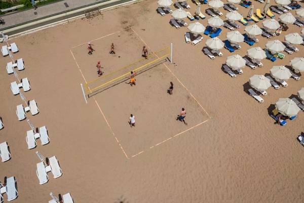 Besuch des Melas Resorts, Leute spielen Volleyball am Strand vor vielen Sonnenliegen