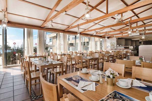 Foto des Innenraums des Restaurants im Europalace Hotel mit Holztischen und Stühlen, Tischblumen und Fenstern mit Blick auf das Meer.