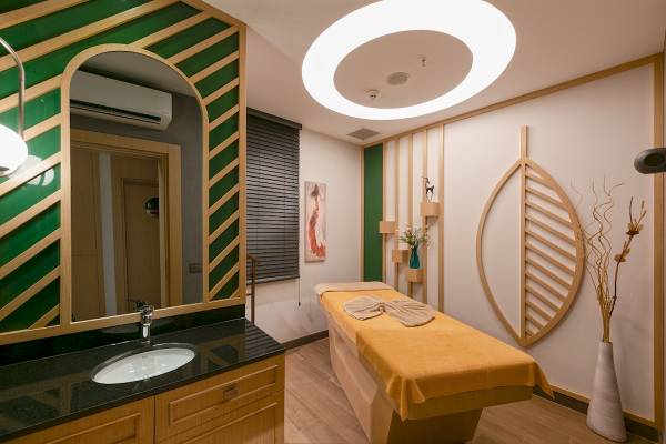 Massageraum im Novum Garden Side Hotel mit gelber Liege, Holzelementen und moderner Einrichtung.