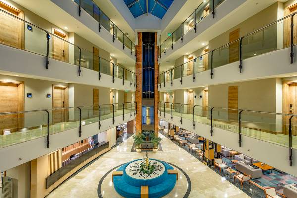 Innenansicht der Lobby des Novum Garden Side Hotel mit mehreren Stockwerken, Aufzügen und Tischen.