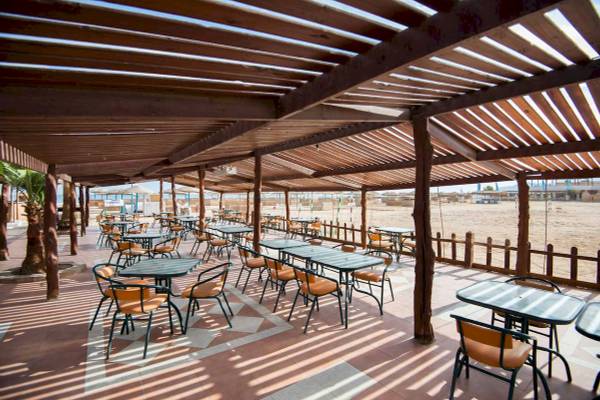 Terrasse des Shams Safaga Resorts mit Tischen und Stühlen unter einem Holzdach.