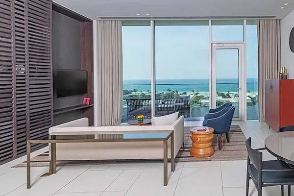 Wohnzimmer des Oberoi Beach Resort Al Zorah mit Meerblick, Couch, Tisch, Stühle und Fernseher.