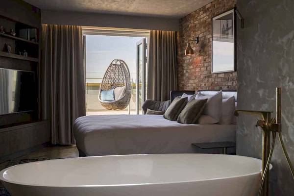 Innenansicht eines Zimmers im Novotel London Canary Wharf mit Bett, Badewanne, Hängesessel und Aussicht.