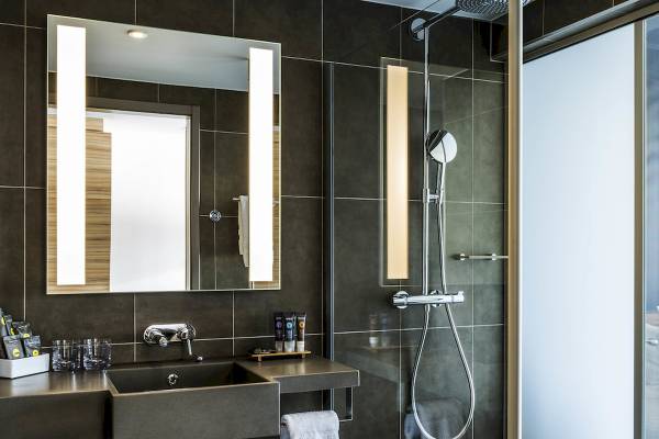 Badezimmer des Novotel London Canary Wharf mit Waschbecken, Spiegel und Dusche.
