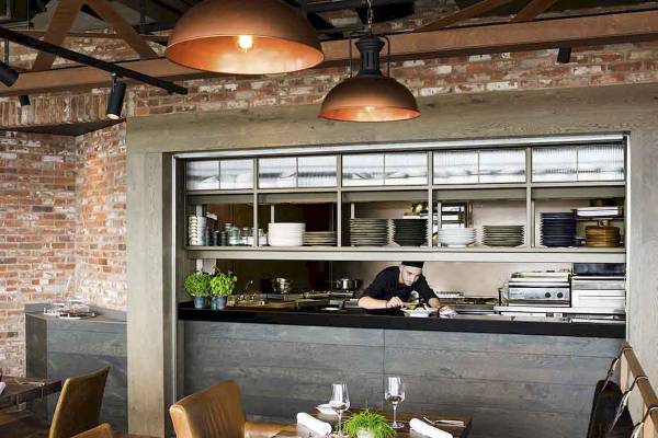 Innenansicht des Restaurants im Novotel London Canary Wharf mit Koch hinter der Theke und eingerichteten Tischen.