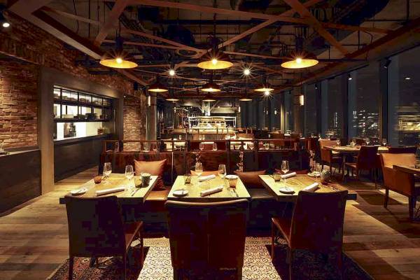 Innenansicht des Restaurants im Novotel London Canary Wharf mit Tischen und Stühlen, Beleuchtung und Holzboden.