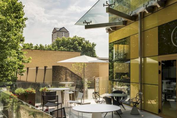 Terrasse des Novotel London Canary Wharf mit Tischen, Stühlen und Schirmen.