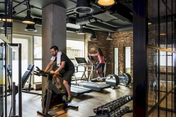 Fitnessstudio im Novotel London Canary Wharf mit Mann auf Fahrrad und Frau auf Laufband.