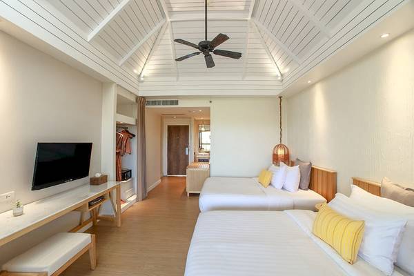 Innenansicht eines Zimmers im Bandara Resort & Spa, Samui mit zwei Betten, Fernseher, Schreibtisch und Deckenventilator.