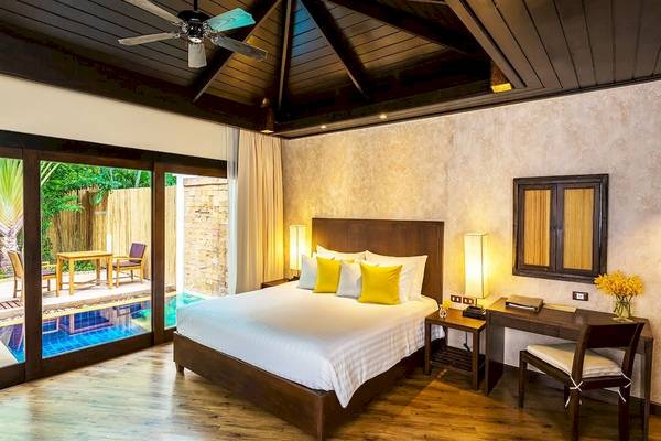 Ein Schlafzimmer im Bandara Resort & Spa, Samui, mit einem Bett, einem Schreibtisch und einem Swimmingpool im Hintergrund.