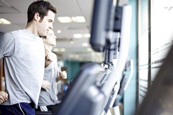 Ein Mann läuft auf einem Laufband im Fitnessstudio, während ein anderer Mann im Hintergrund läuft.