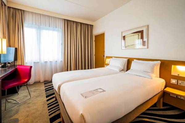 Zwei Betten in einem modernen Hotelzimmer im Novotel London West mit Schreibtisch und Stuhl.