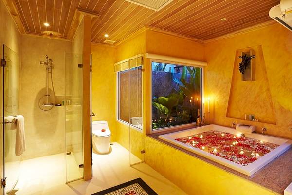 Badezimmer im Bandara Resort & Spa, Samui mit Badewanne, Kerzen und Blütenblättern.