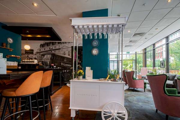 Innenbereich des Novotel London West mit einem Champagnerwagen, Barhockern und Möbeln.