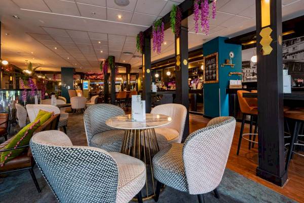 Innenbereich des Novotel London West mit Möbeln, Tischen und hängenden Blumen.
