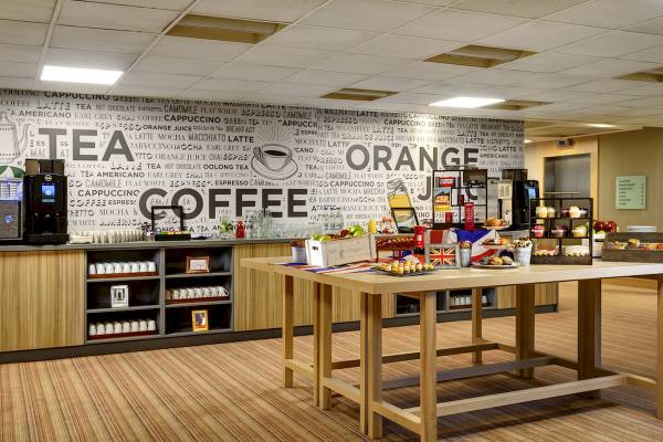 Barbereich im Novotel London West Hotel mit einer Wand voller Kaffeenamen und einer Theke mit verschiedenen Getränken und Speisen.