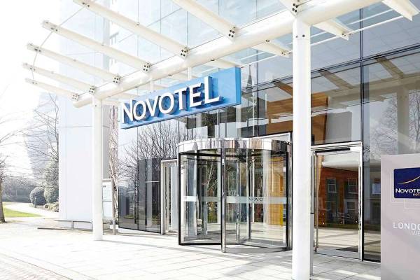 Eingangsbereich des Novotel London West mit modernem Glasgebäude und rotierenden Drehtüren.