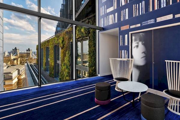 Innenansicht des DoubleTree by Hilton Tower of London mit blauen Wänden, Bücherregal, Fenster und Blick auf die Stadt.