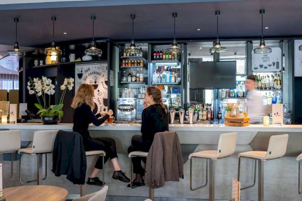 Hotelbar im Novotel Paris Centre Bercy mit zwei Frauen an der Bar und einer Person im Hintergrund.