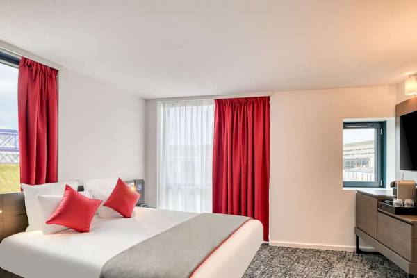 Ein modernes Hotelzimmer im Novotel Paris Centre Bercy mit einem Bett, roten Vorhängen und einer Aussicht.