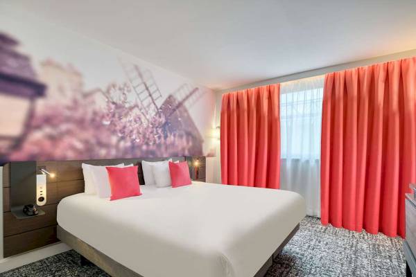 Hotelzimmer im Novotel Paris Centre Bercy mit weißem Bett, roten Vorhängen und Wandbild.